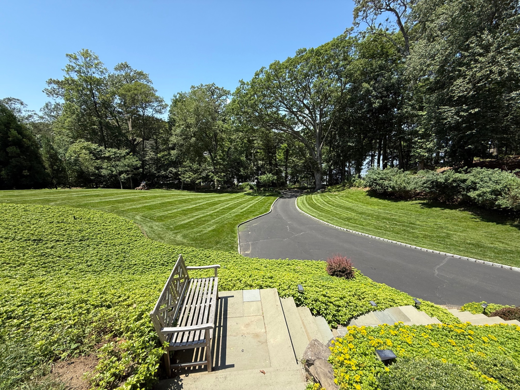 Striped freshly mowed lawn beside a clean cobble-edged driveway and groundcover beds
