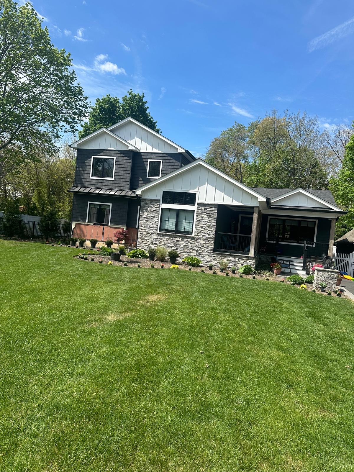 Freshly mowed green lawn in front of a two-story home with newly planted flower beds and stone edging